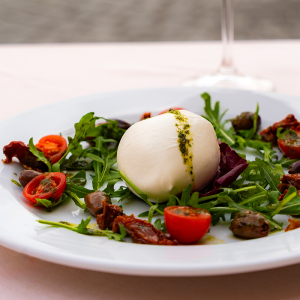 Bufala di Pæstum mozzata a mano su letto di rucola con pomodorini, pomodori secchi, olive taggiasche e salsa di basilico